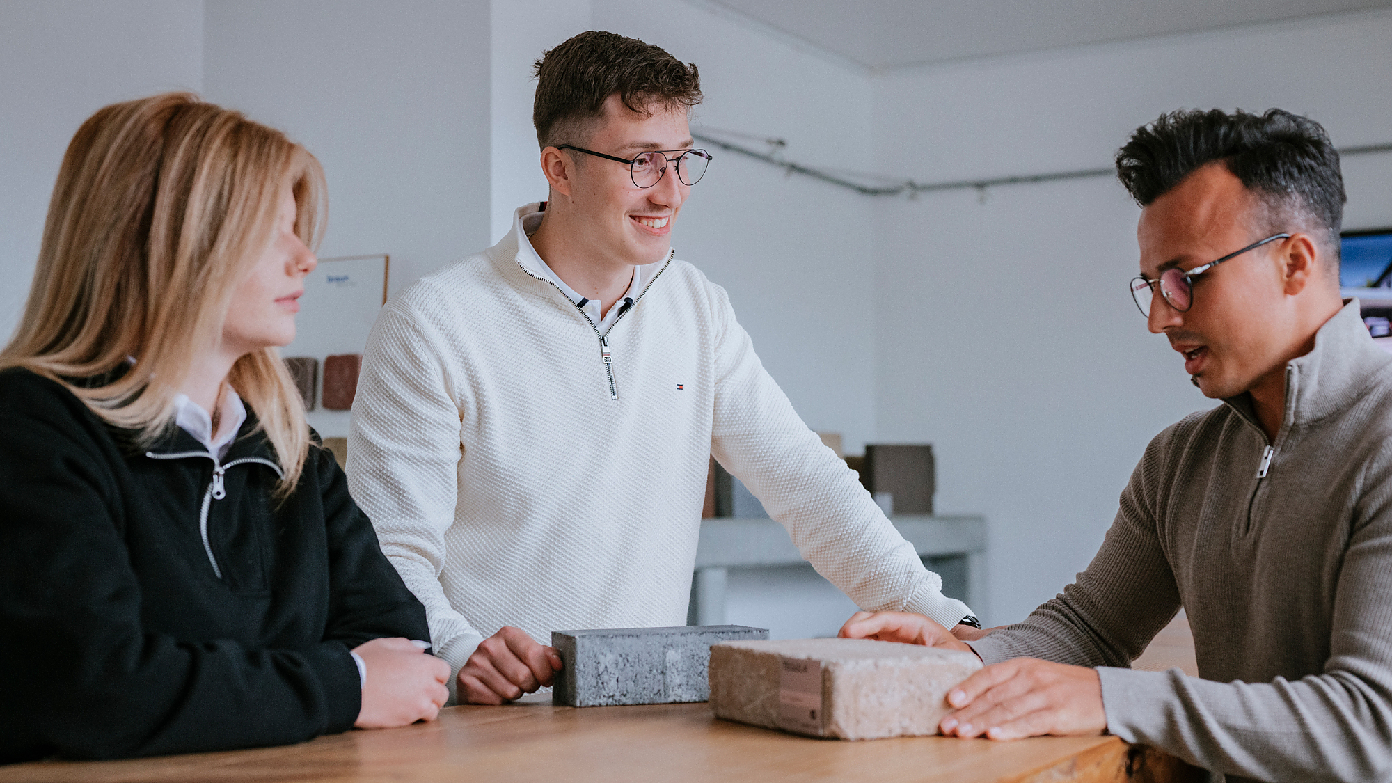 Zwei junge Männer und eine junge Frau stehen an einem Tisch