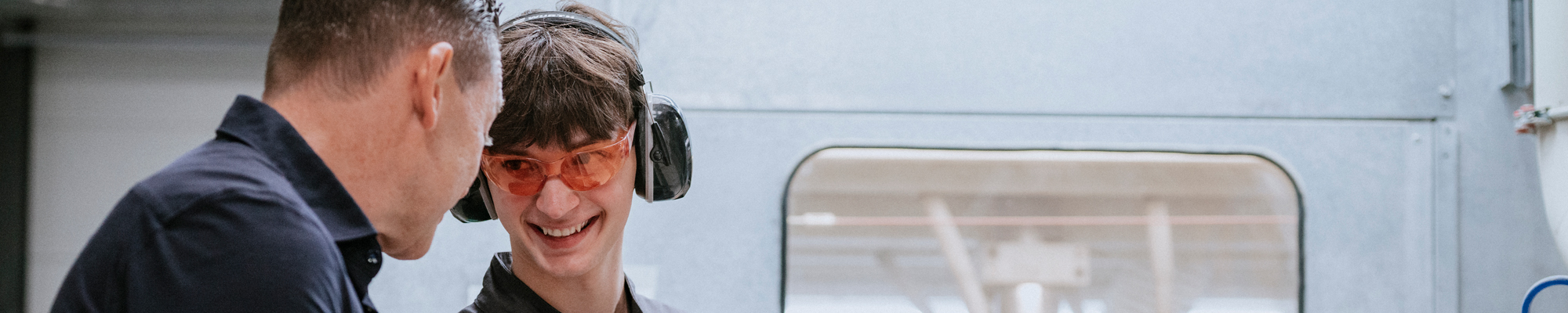 Ein Azubi lässt sich an einer Maschine etwas von seinem Ausbilder erklären