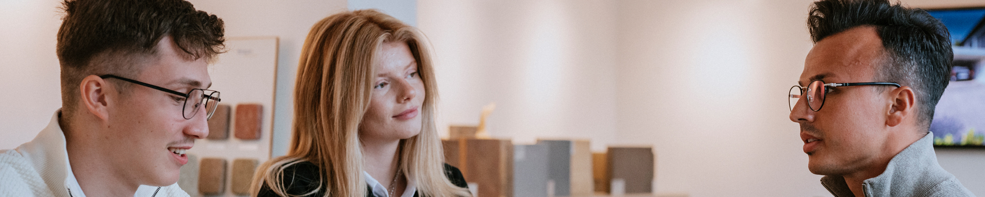 Zwei Männer und eine junge Frau unterhalten sich an einem Tisch