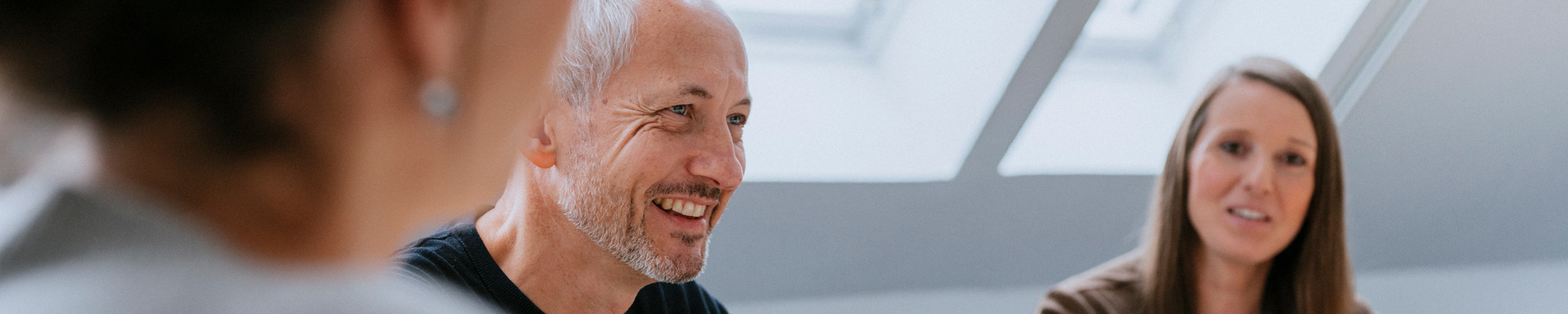 Ein Mann und zwei Frauen sitzen an einem Besprechungstisch.