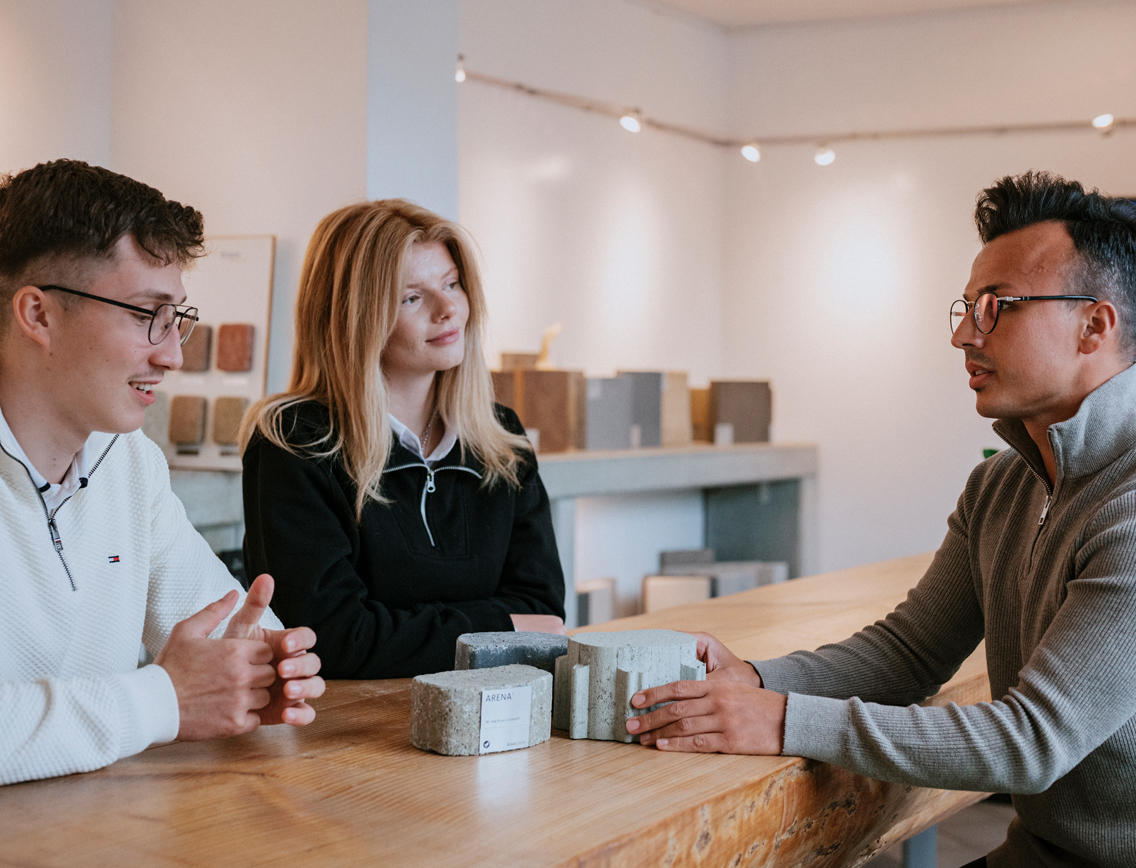 Zwei junge Männer und eine junge Frau unterhalten sich an einem Tisch