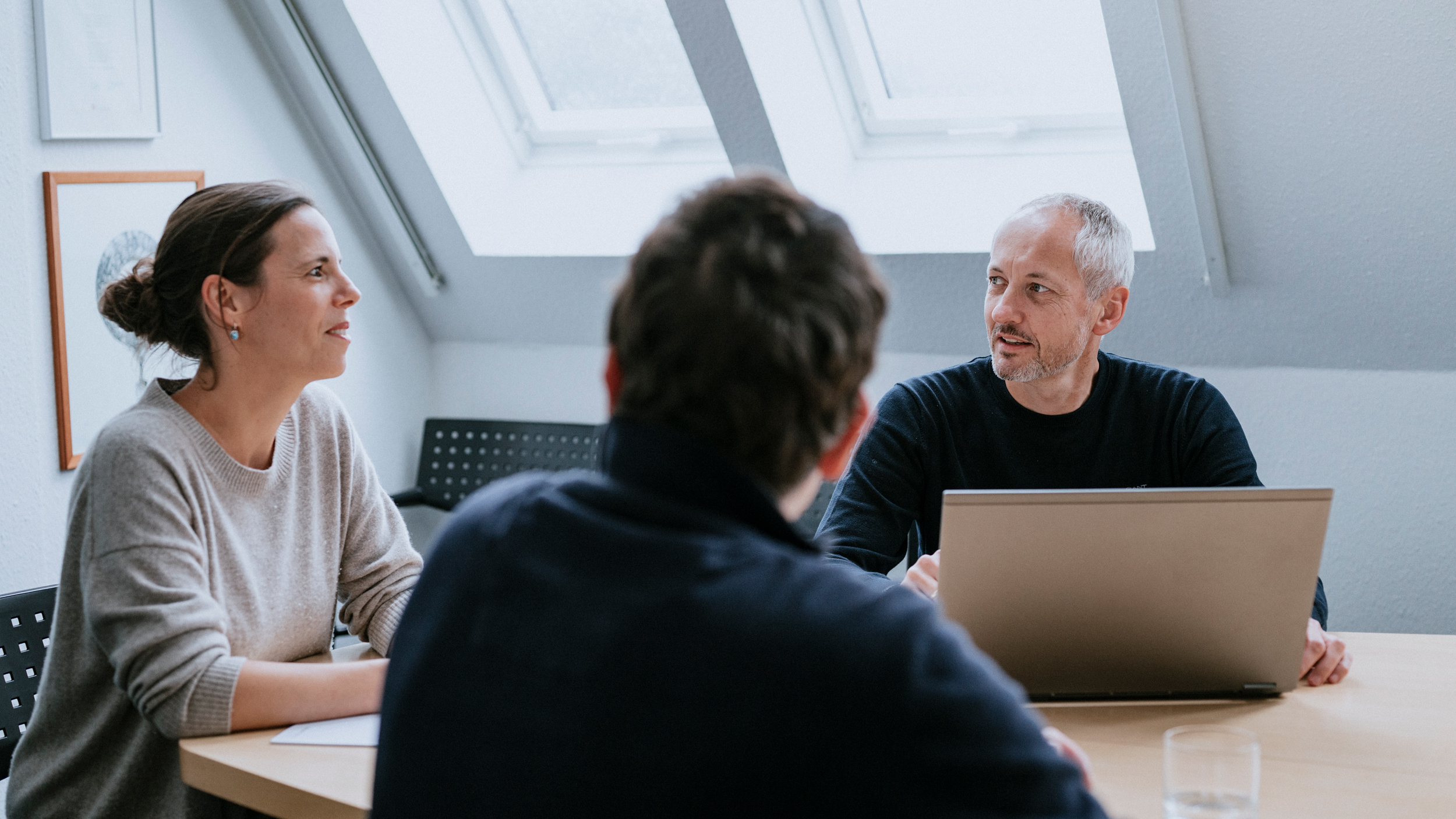 Zwei Männer und eine Frau sitzen an einem Besprechungstisch