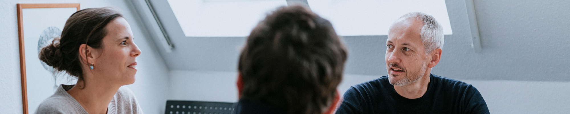 Zwei Männer und eine Frau sitzen an einem Besprechungstisch